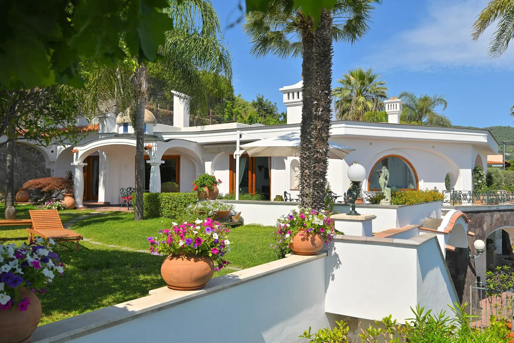 The white arches of the villa among the palms and the flowering pots