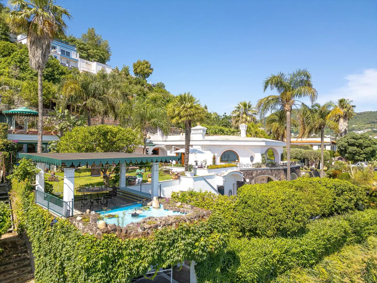 The estate seen by drone: the white villa, the pool and the gardens above the bay