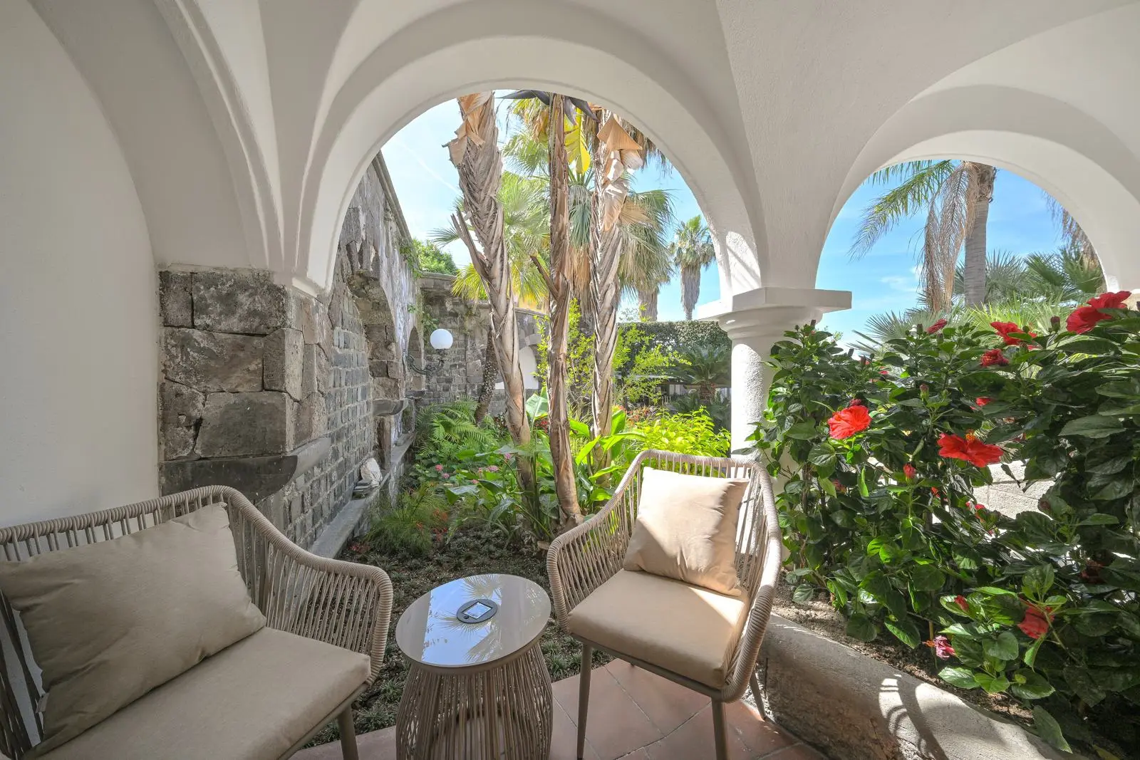 Wicker armchairs on the stone patio beneath the arches